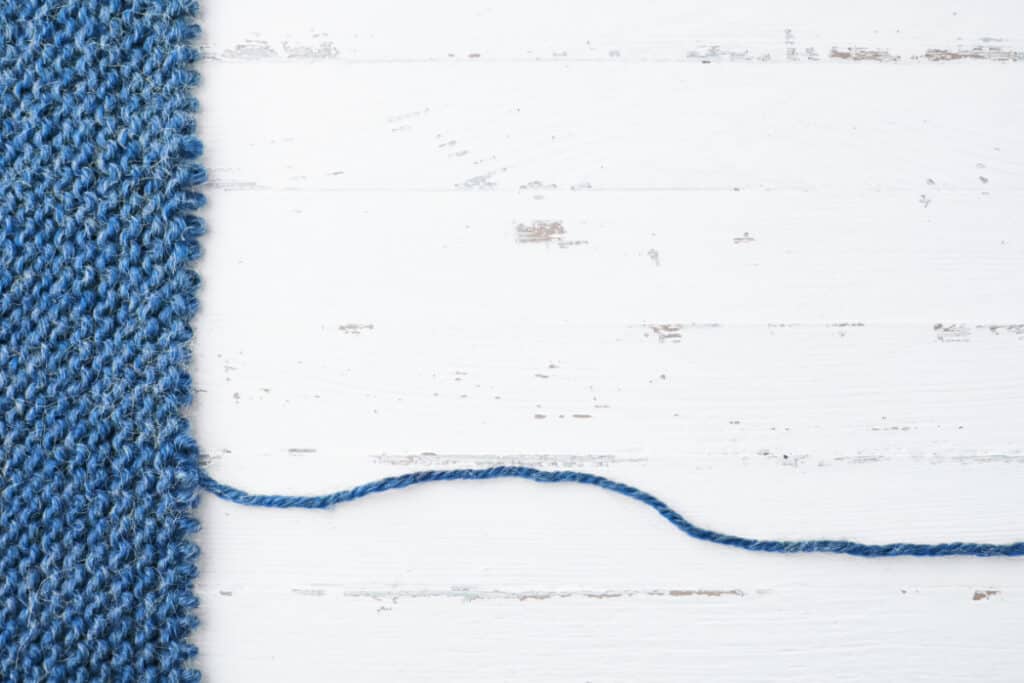 blue knitted sweater unraveling on white background