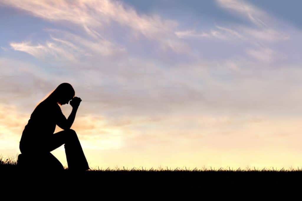 parent bowing her head in prayer, silhouette at sunset