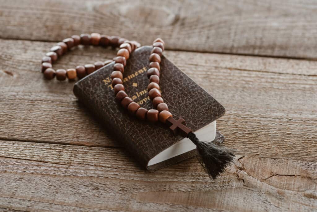 small black new testament with rosary on top, sitting on wooden table