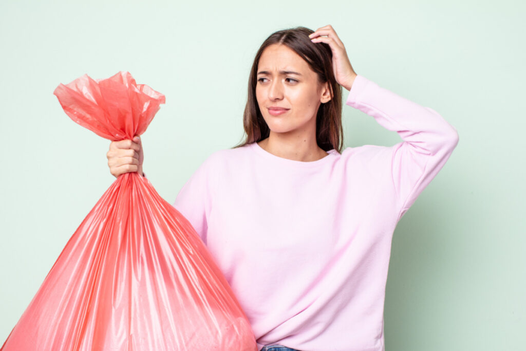 woman holding trash bag looking confused and scratching her head.