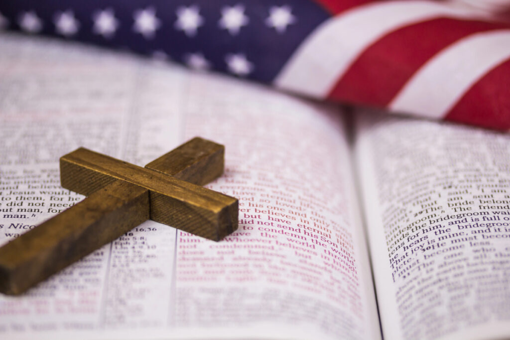 open Bible with small wooden cross and an American flag overlay.